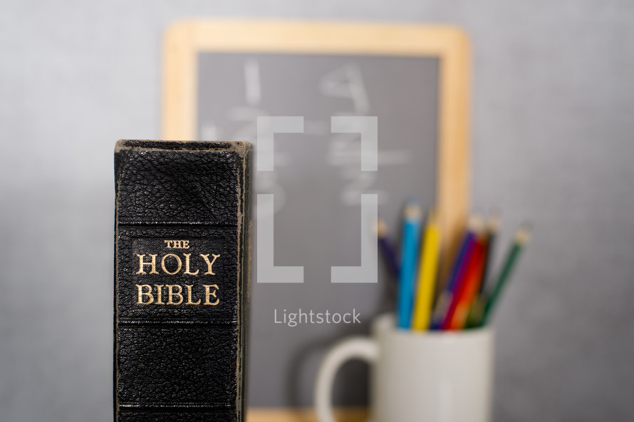 Holy Bible, colored pencils in a mug, and a blackboard
