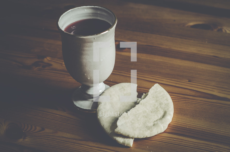 A cup of wine and broken bread on a wooden table.