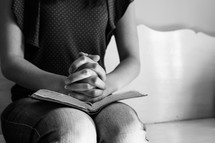 a teen girl with praying hands over a Bible 
