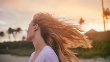 a woman tossing her hair on a beach at sunset 