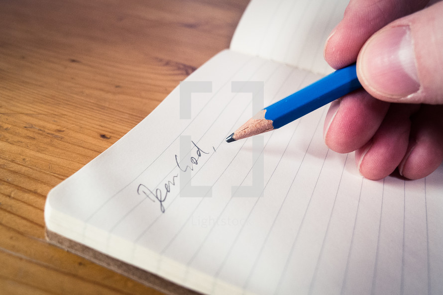 A male hand writing with a blue pencil in an open notebook with the words 'dear God'.