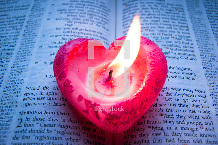 A pink heart-shaped candle burns on a bible opened at Luke chapter 2.
