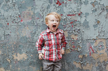 boy child yelling in front of a wall with peeling paint 