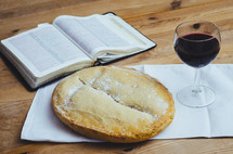 An open bible, loaf of bread and glass of wine on a table