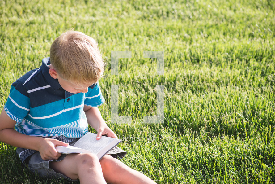 a boy reading a Bible in the grass 