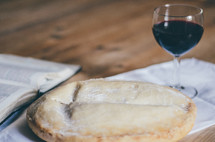 A loaf of bread, glass of wine and open bible on a table