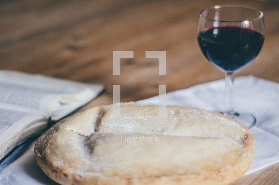 A loaf of bread, glass of wine and open bible on a table