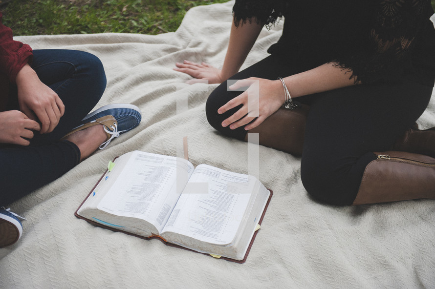 a teenage girl sitting on a blanket reading a Bible 