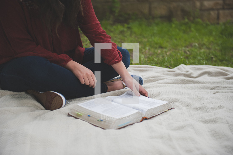 a teenage girl sitting on a blanket reading a Bible 