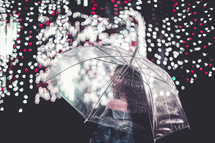 a woman standing under an umbrella and raining Christmas lights 