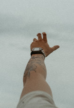 Man with tattoo reaching for the sky