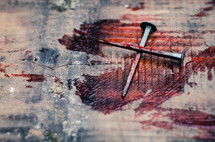Two bloody nails form a cross on a blood covered wooden beam