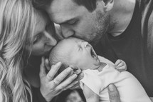 new parents kissing their newborn 