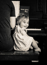 Baby girl listens and smiles while dad plays worship music on the piano.