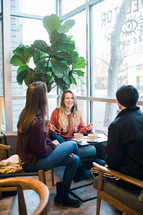 small group of young adults sitting in a window seat talking over coffee 