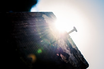 the sun's rays are seen behind a nail hammered into an old wooden cross beam