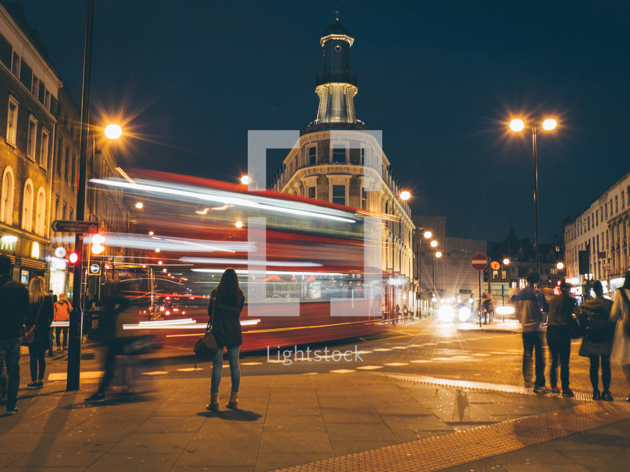 A red london bus driving through a city intersection at night