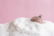 Rose gold bauble in powdery snow on a pink background