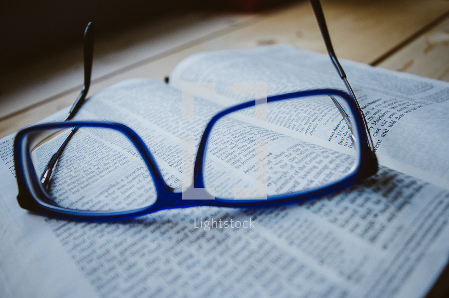 A pair of blue glasses sit atop an open bible.