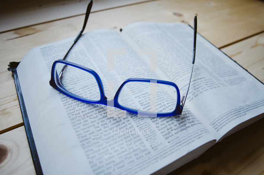 A pair of blue glasses sit atop an open bible
