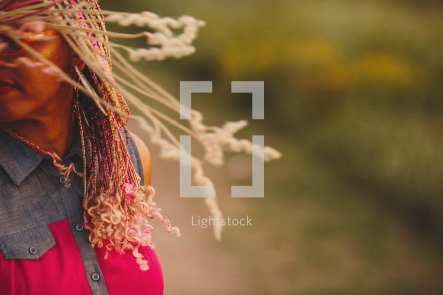 African-American woman with pink and blonde braids twirling her hair outdoors 