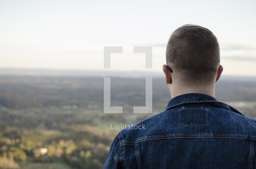 man standing with his back to the camera looking out at a valley 