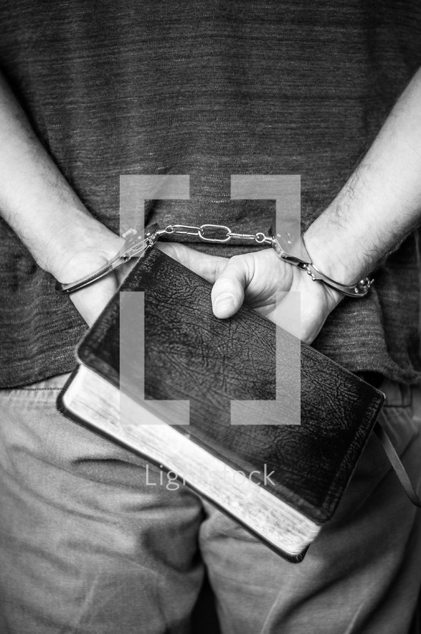 handcuffed man holding a Bible behind his back 