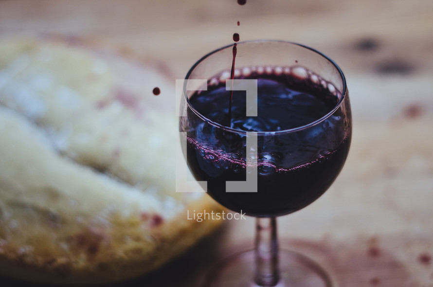 Wine is poured into a glass, next to a loaf of bread on a table