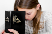 Woman with her head bowed praying while holding a closed Bible.