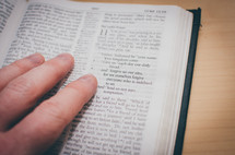 A bible opened to Luke's gospel with fingers pointing to the Lord's prayer