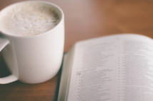 Coffee cup and open Bible on a table.