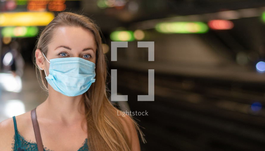a young woman wearing a surgical mask standing in a subway 