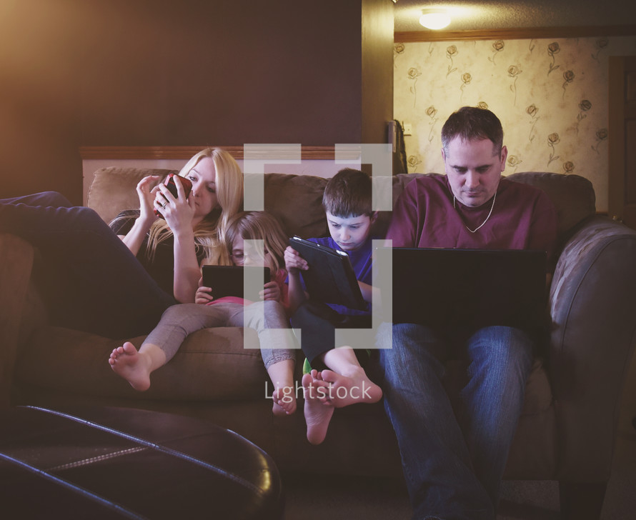 a family sitting on a couch playing electronics 