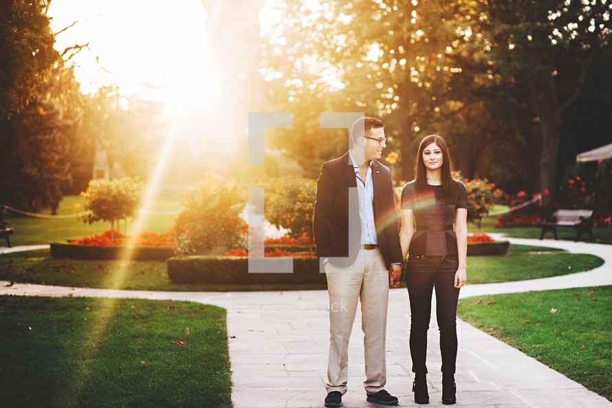 a couple standing on a sidewalk in a garden at sunset 
