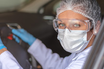 Young doctor or nurse driving car with protective mask on her face. COVID-19. Coronavirus