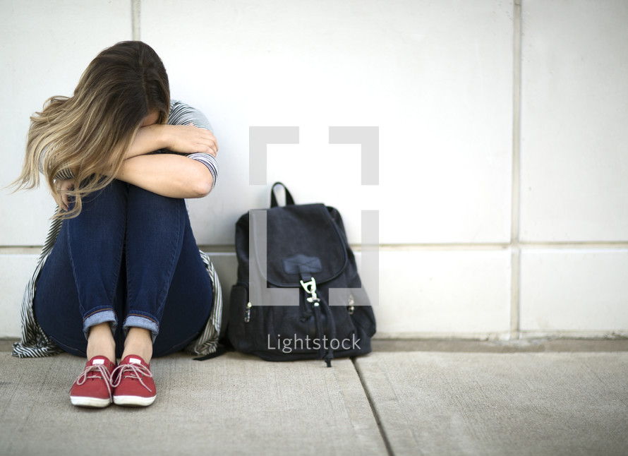 sad girl next to a book bag 
