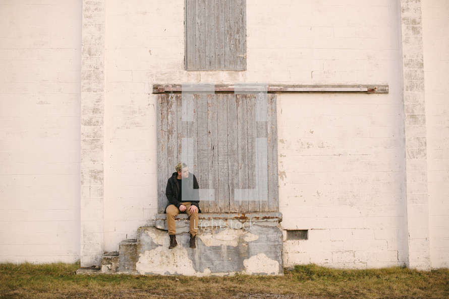 a man sitting on a stoop at the back of a warehouse 