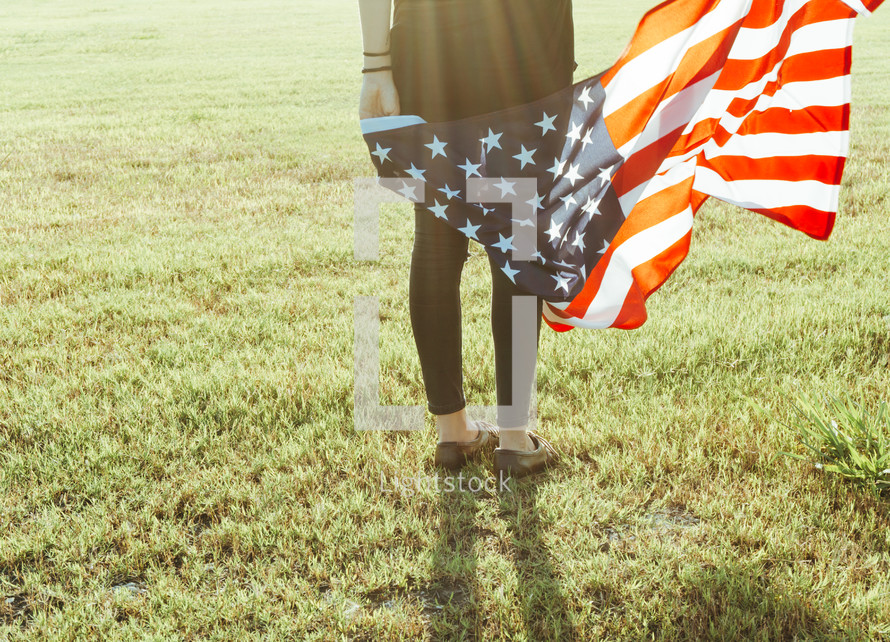 a woman holding an American flag standing in grass 