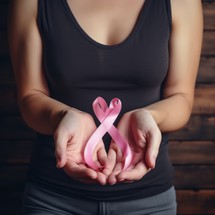 Breast cancer awareness concept. Woman hands holding pink ribbon on wooden background.