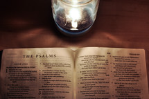 Bible open to The Psalms on a wooden table near a burning candle.