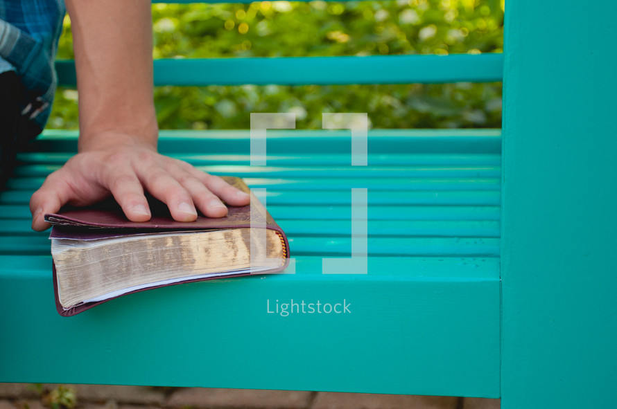 a hand on a Bible on a bench 