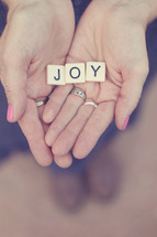 word joy in scrabble pieces in a woman's hands 