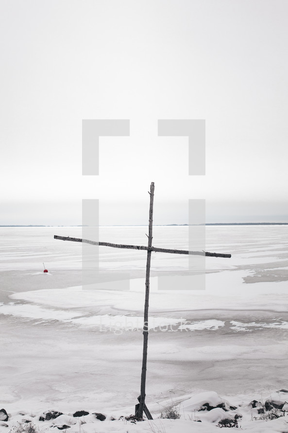 wooden cross by a frozen lake 