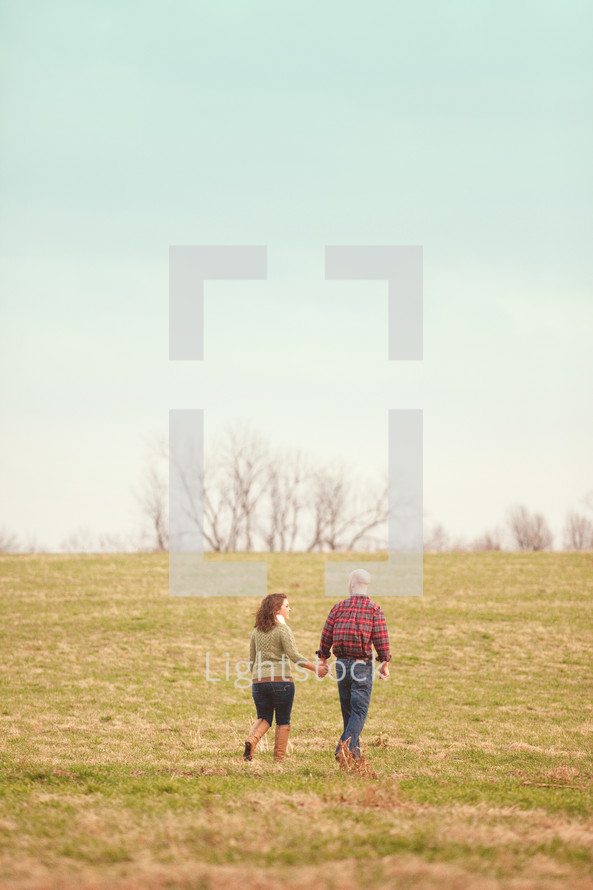 couple walking in a field holding hands 