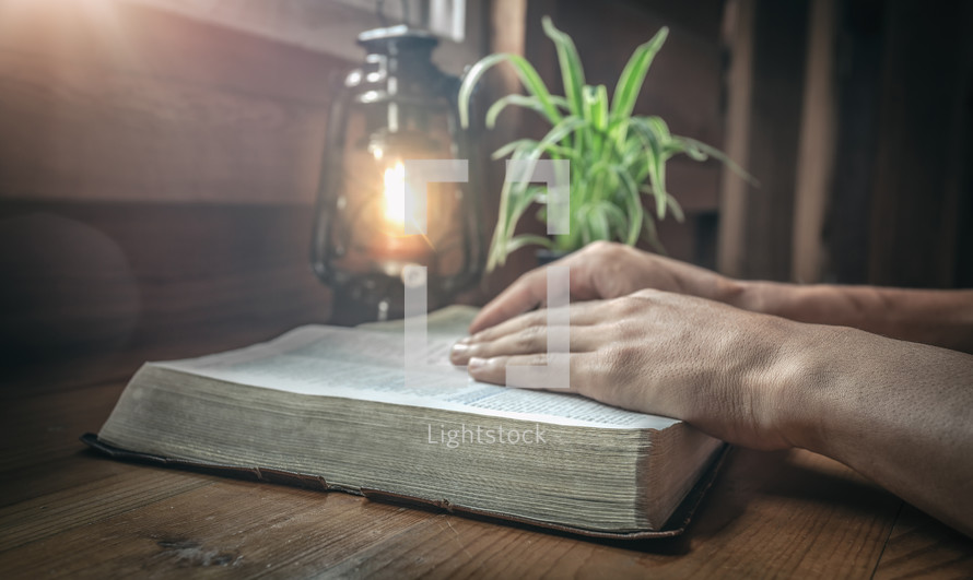 person reading a Bible by the light of an oil lamp 