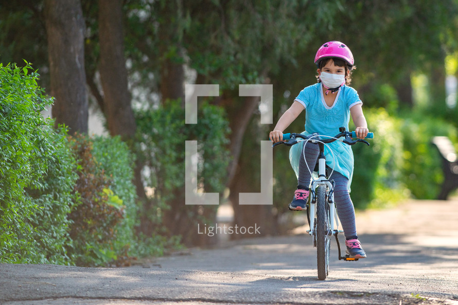 Little girl in protective medical mask rides a bicycle.