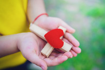 Close up hands of child girl holding cross with red heart in hand, love of jesus concept.