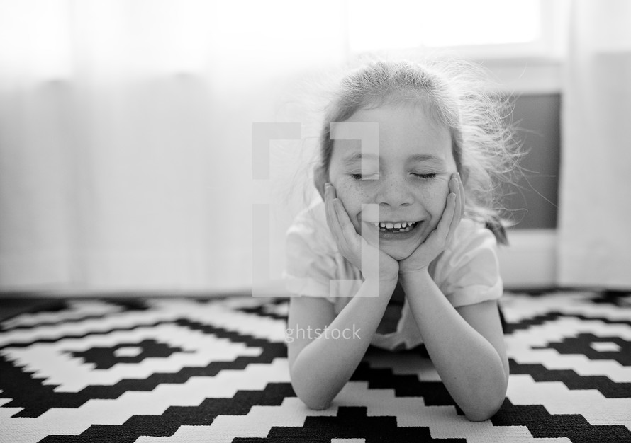 a smiling kid with hands under her chin 
