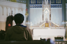 A young man praying in a large Catholic church