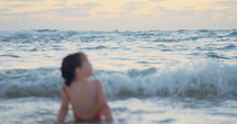 Little girl playing on the beach in the water during sunset hour
